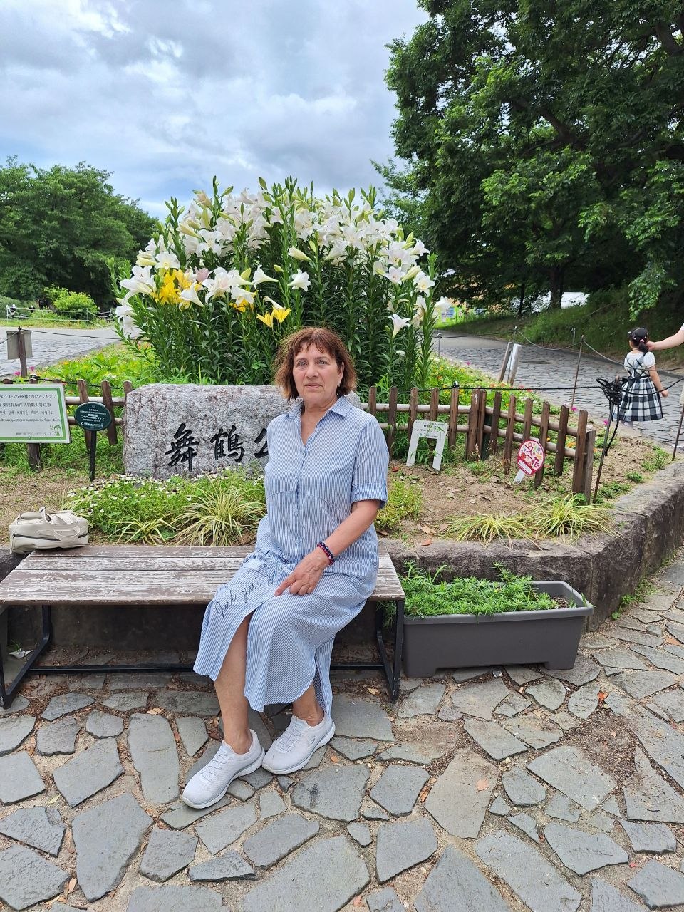 Галина на скамейке у клумбы с белыми лилиями в парке Майдзуру, Япония